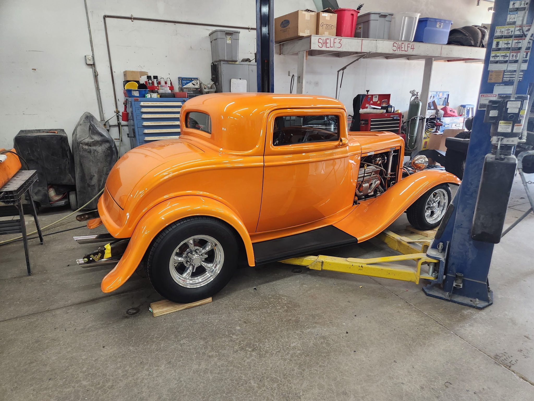 Bright orange classic car on a hydraulic lift inside an auto body shop with tools and equipment in the background, representing collision repair and auto body services in Cedar Rapids and nearby communities.