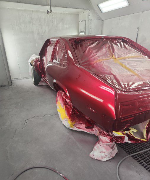 Kelleys Auto Body Red car undergoing professional collision repair and paintwork in an auto body shop spray booth, reflecting Kelley’s Auto Body commitment to quality service for Cedar Rapids and nearby communities.